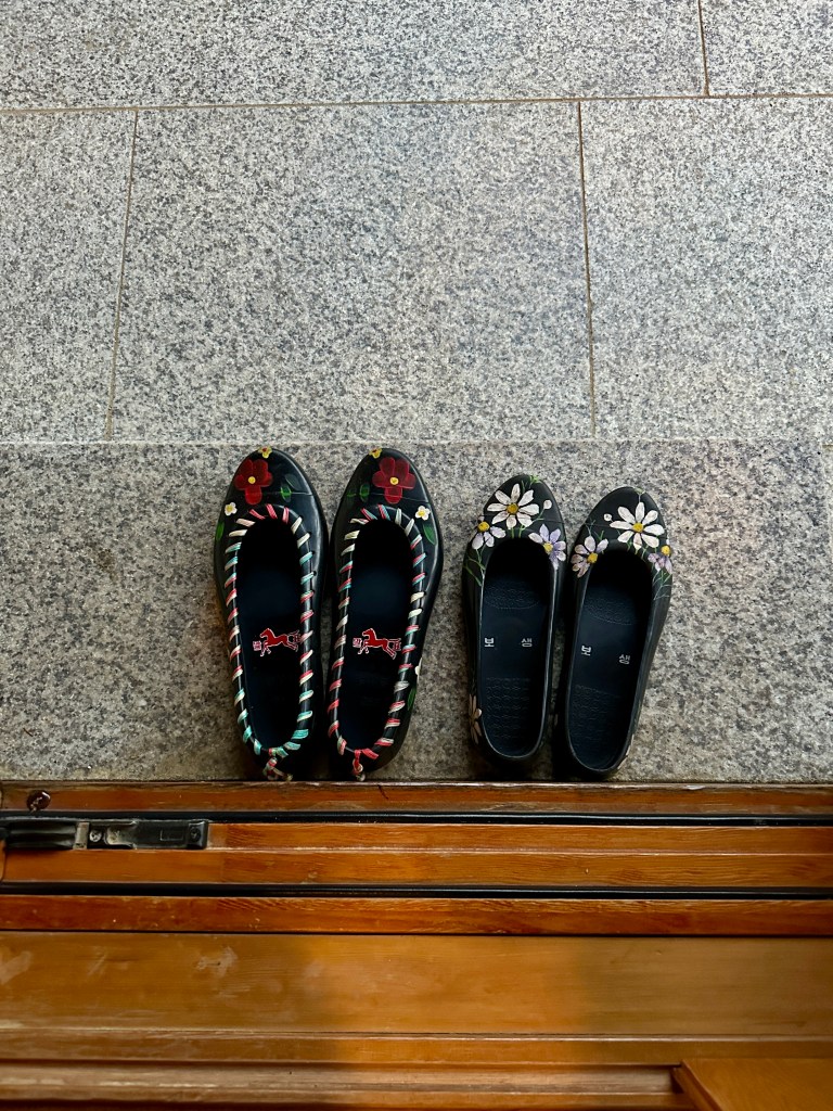 A top-down view of two pairs of traditional Korean shoes on a stone floor, showcasing intricate floral designs and vibrant colors.
